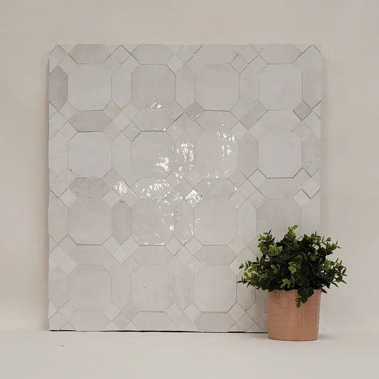 White handcrafted Zellige mosaic tile panel with geometric octagon and diamond pattern, displayed with a small potted plant for scale.