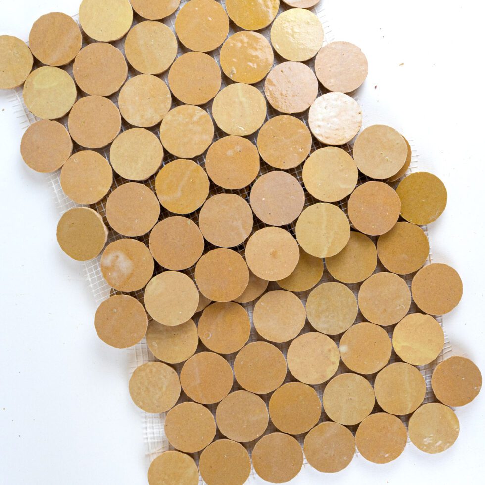 Close-up of round amber color zellige mosaic tiles arranged in a pattern on a white background