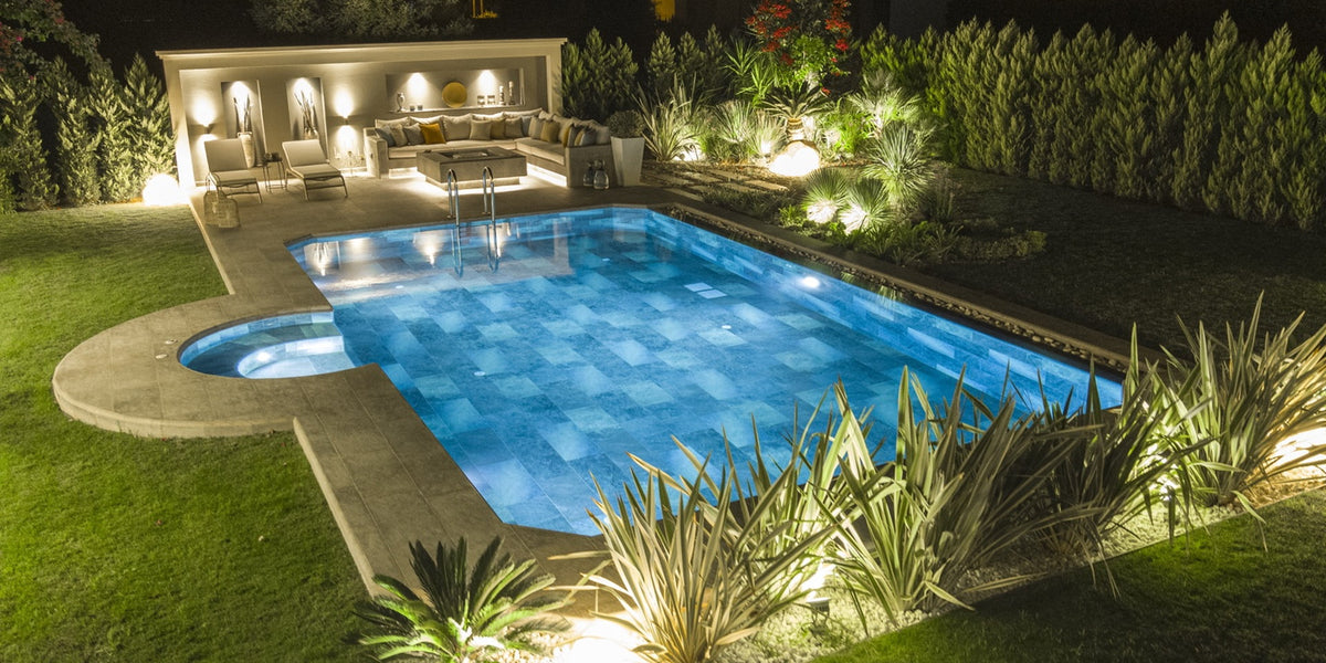 Luxury outdoor living environment with an illuminated swimming pool, landscaped garden, and coordinated poolside surfaces