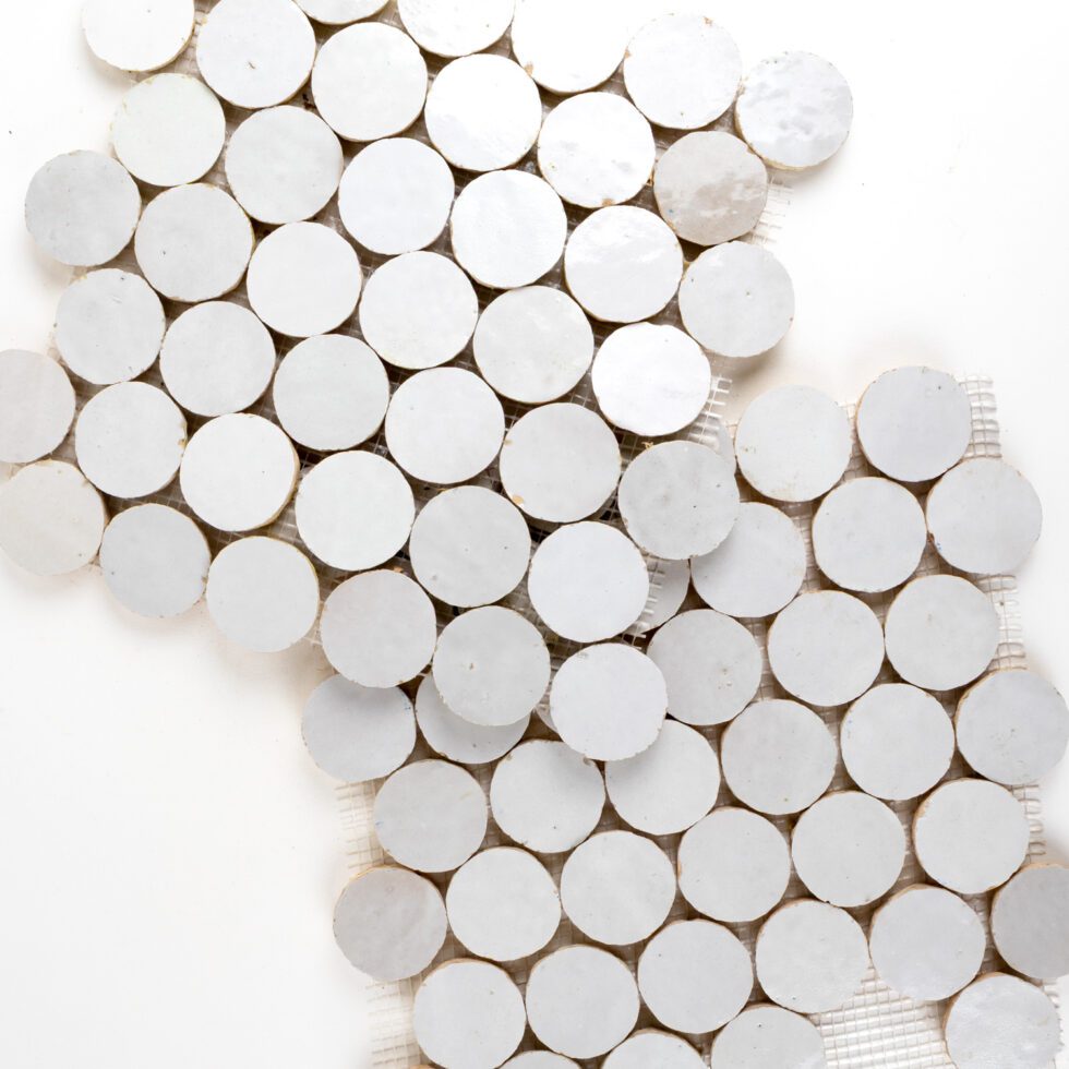 Close-up of white circular zellige mesh-mounted tiles arranged in a pattern on a white background