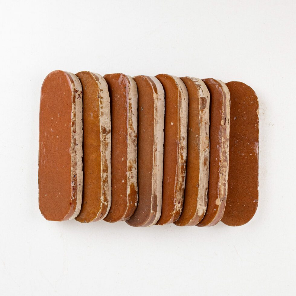 Row of oval shaped brown terracotta color zellige tiles on a white background
