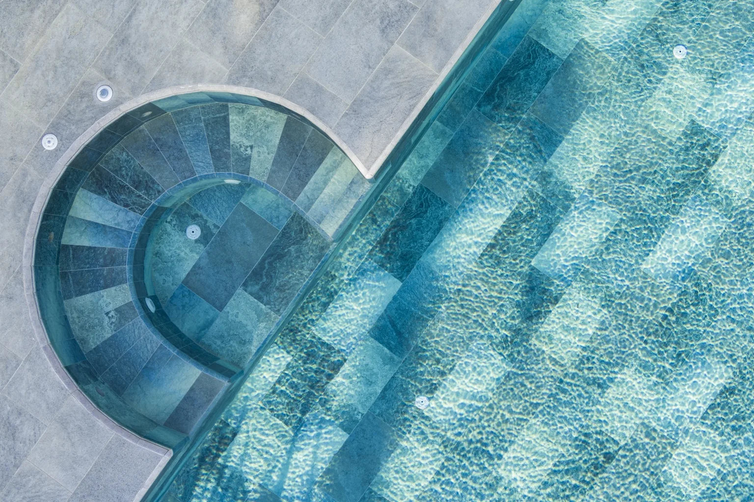 SeraPool Relax pool & spa installation showing curved spa steps with blue-green porcelain pool tile and gray pool deck coping