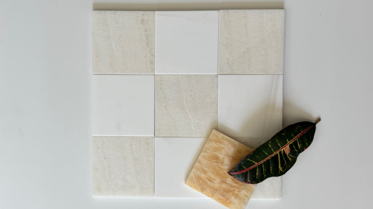 Bianco Dolomite and Vanilla Onyx tiles arranged in a checkerboard pattern, with a dark green leaf adding a natural touch. The mix of creamy beige and pure white tiles creates a luxurious and elegant look, perfect for modern tile designs.