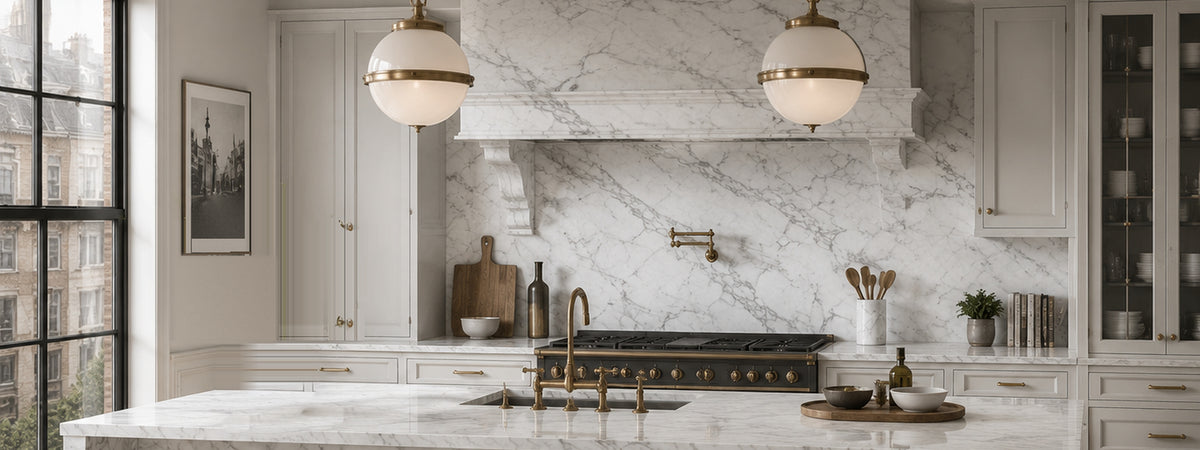Classic kitchen with Carrara white marble island, backsplash and range hood, brass pendant lights and light gray cabinetry