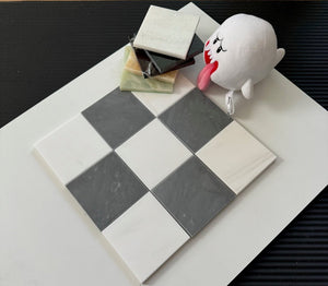 A playful arrangement of checkerboard tiles made from Bardiglio Imperial and Bianco Dolomite marbles, alongside stacked marble tile samples and a soft plush toy. The image showcases marble’s versatility in home design projects, from tile accents to luxurious stone flooring