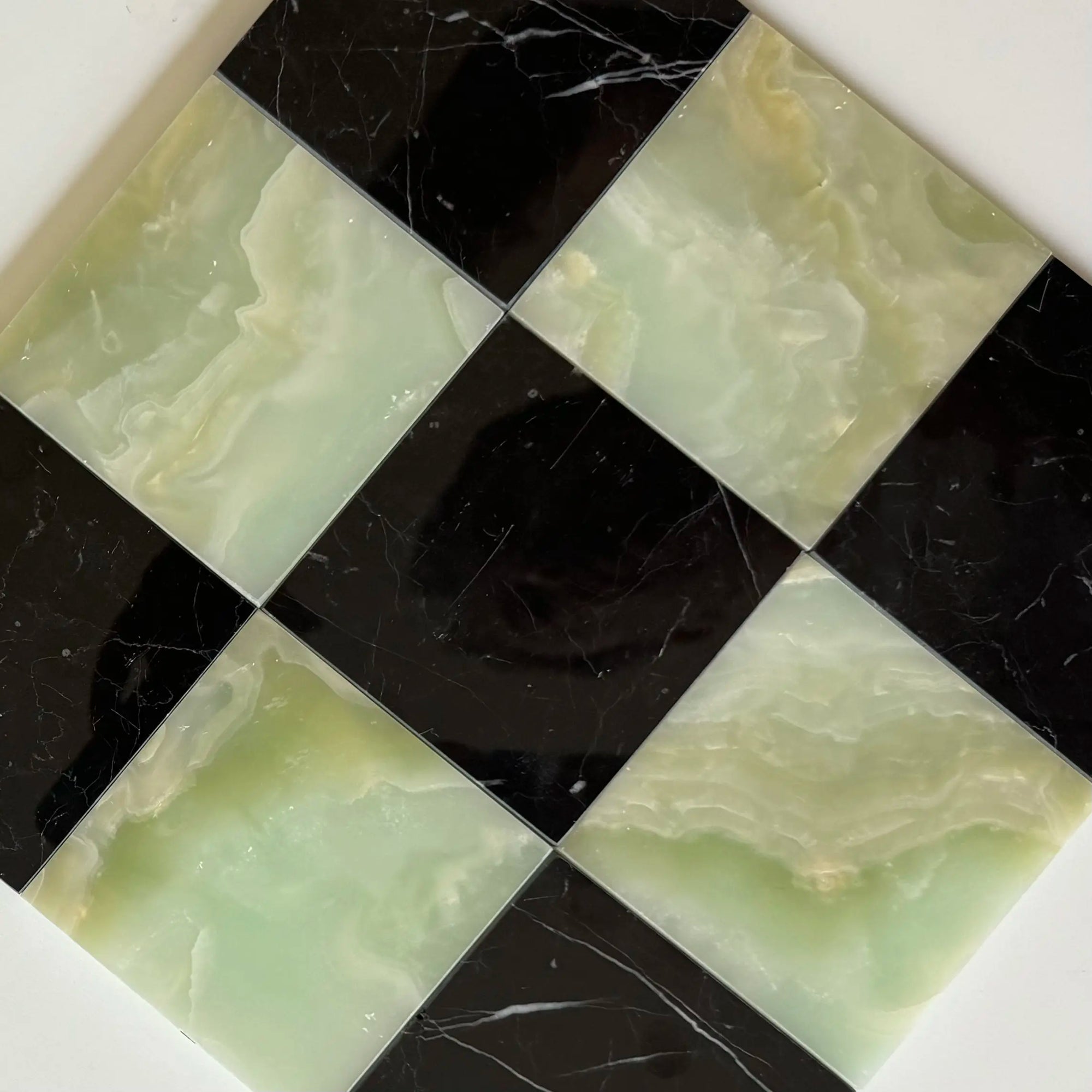 Elegant checkerboard tile layout featuring Nero Marquina black marble paired with Green Onyx stone. The contrasting colors of deep black and translucent green create a striking pattern, perfect for modern interior designs and high-end spaces.