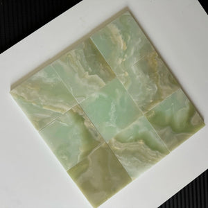 A close-up of nine Green Onyx stone tiles arranged in a smooth, seamless grid pattern. The soft green hues and natural veining of the onyx provide a luxurious feel, ideal for bathroom or kitchen tiling projects.