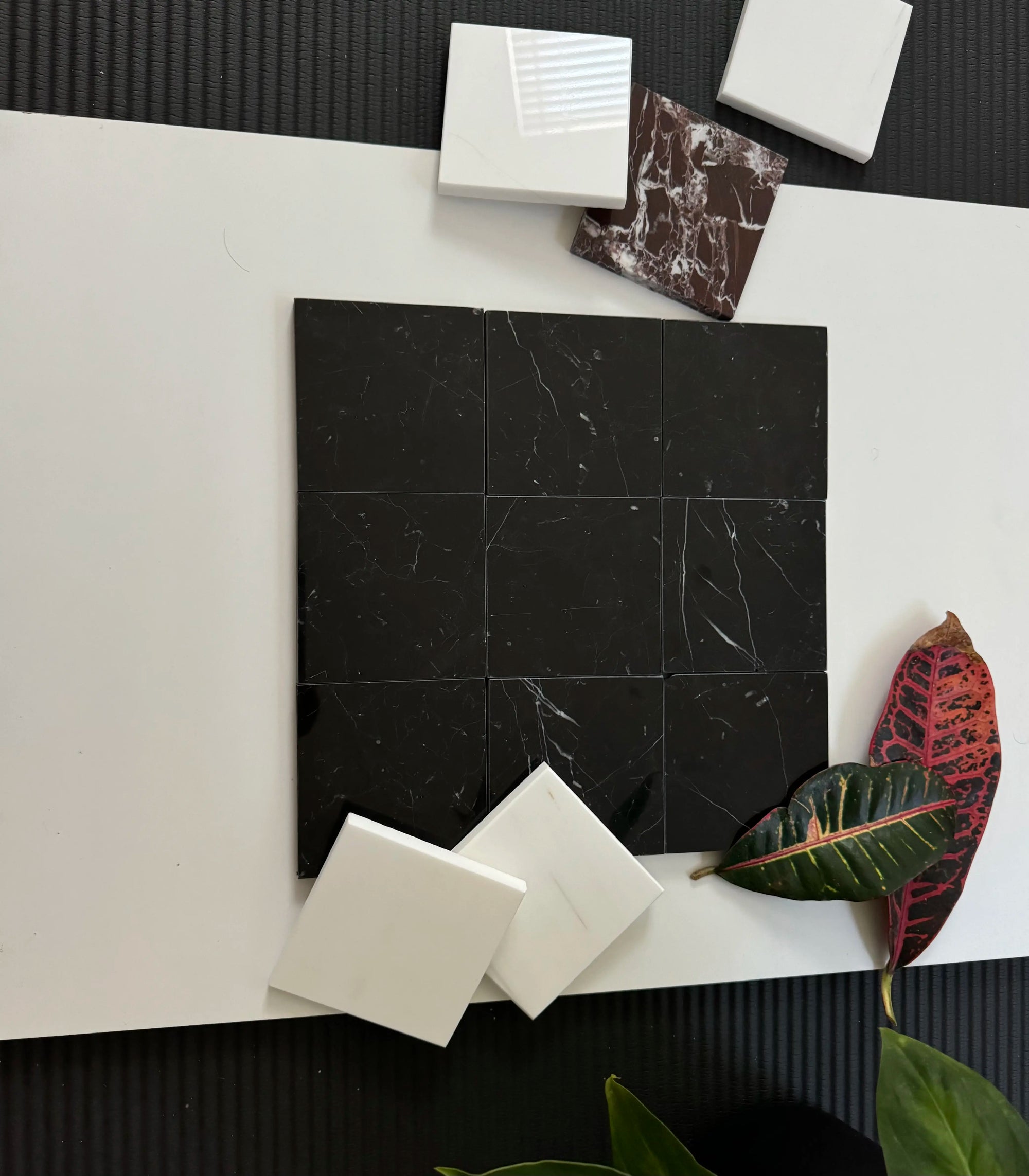 A sleek display of Nero Marquina marble tiles arranged in a grid pattern. The deep black surface is highlighted by fine white veining, perfect for adding a luxurious touch to any design project, from countertops to floors.