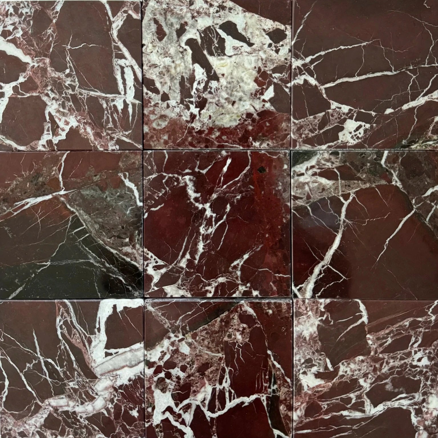 Close-up of Roso Levanto marble tiles arranged in a grid layout. The deep red color of the marble, with bold white veining