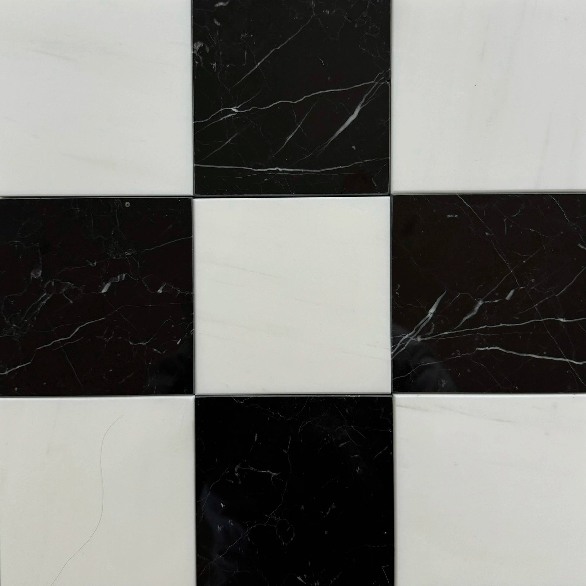 A close-up of a checkerboard tile layout with alternating squares of sleek black Nero Marquina marble and crisp white Bianco Dolomite marble. The contrasting black and white marble create a classic, elegant design ideal for both modern and traditional interiors.