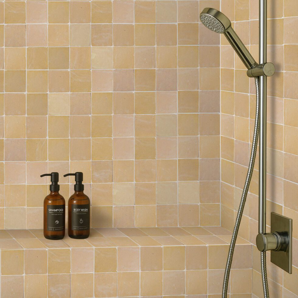 Bathroom shower setup with 4x4 zellige tiled wall, shower head, and bottles on a ledge.